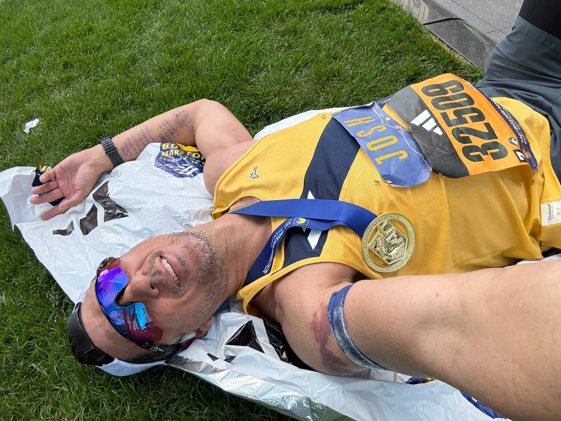 Josh resting on the grass with his medal after the Boston Marathon