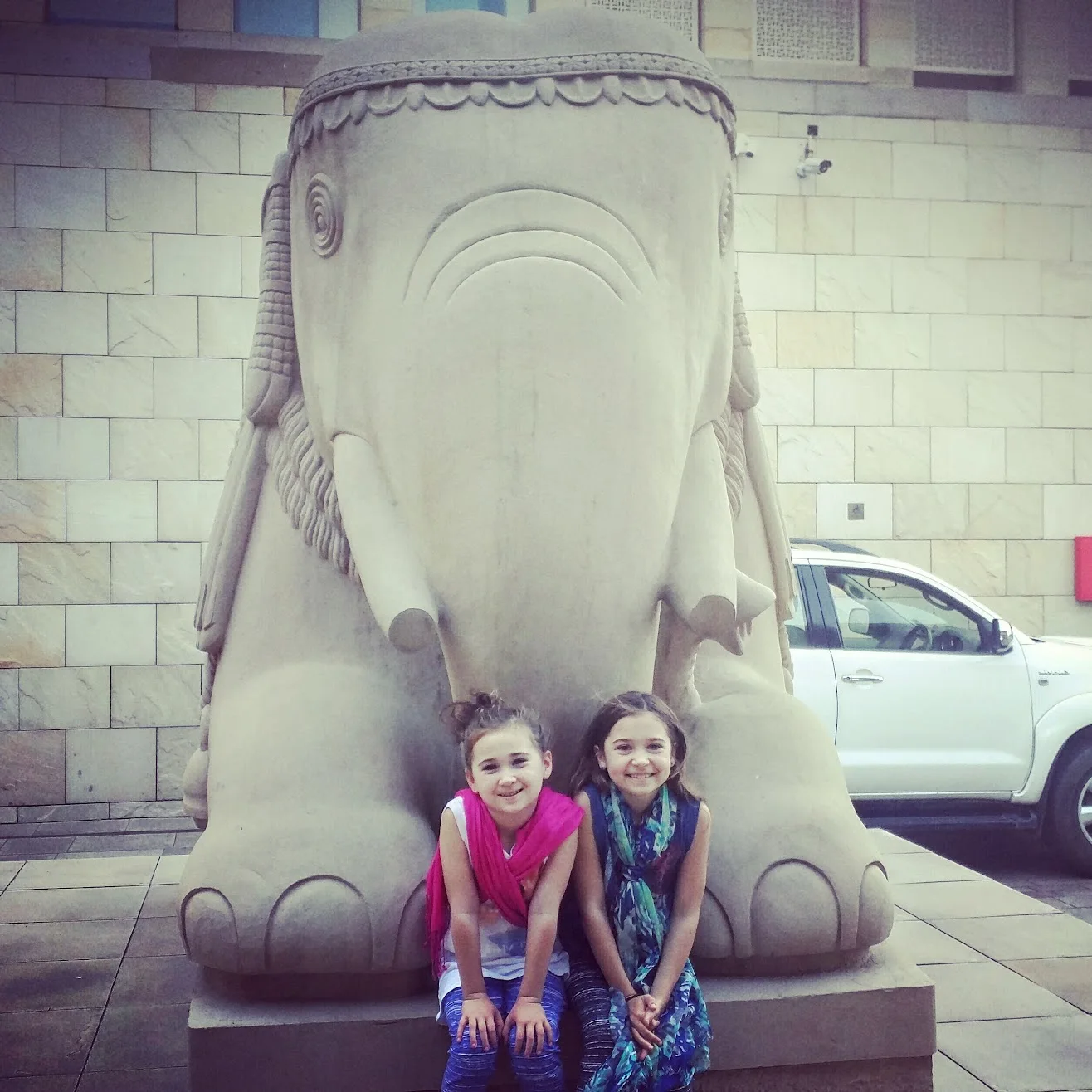 Two sisters sitting beside a carved elephant statue