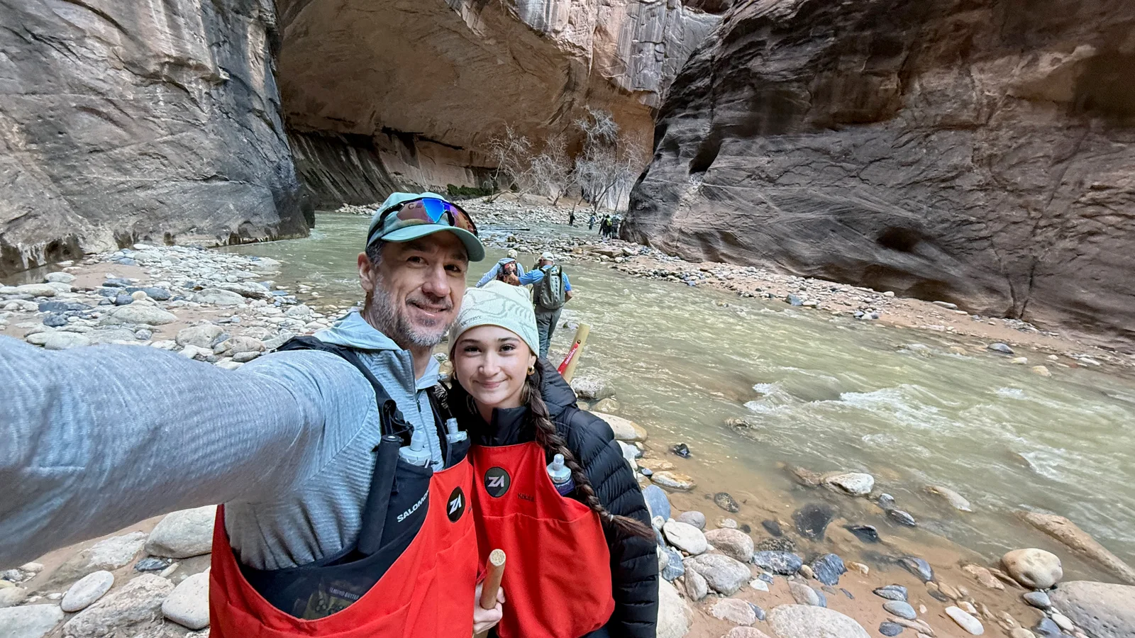 Josh and Lyla beside the river in The Narrows wearing red waterproof bibs